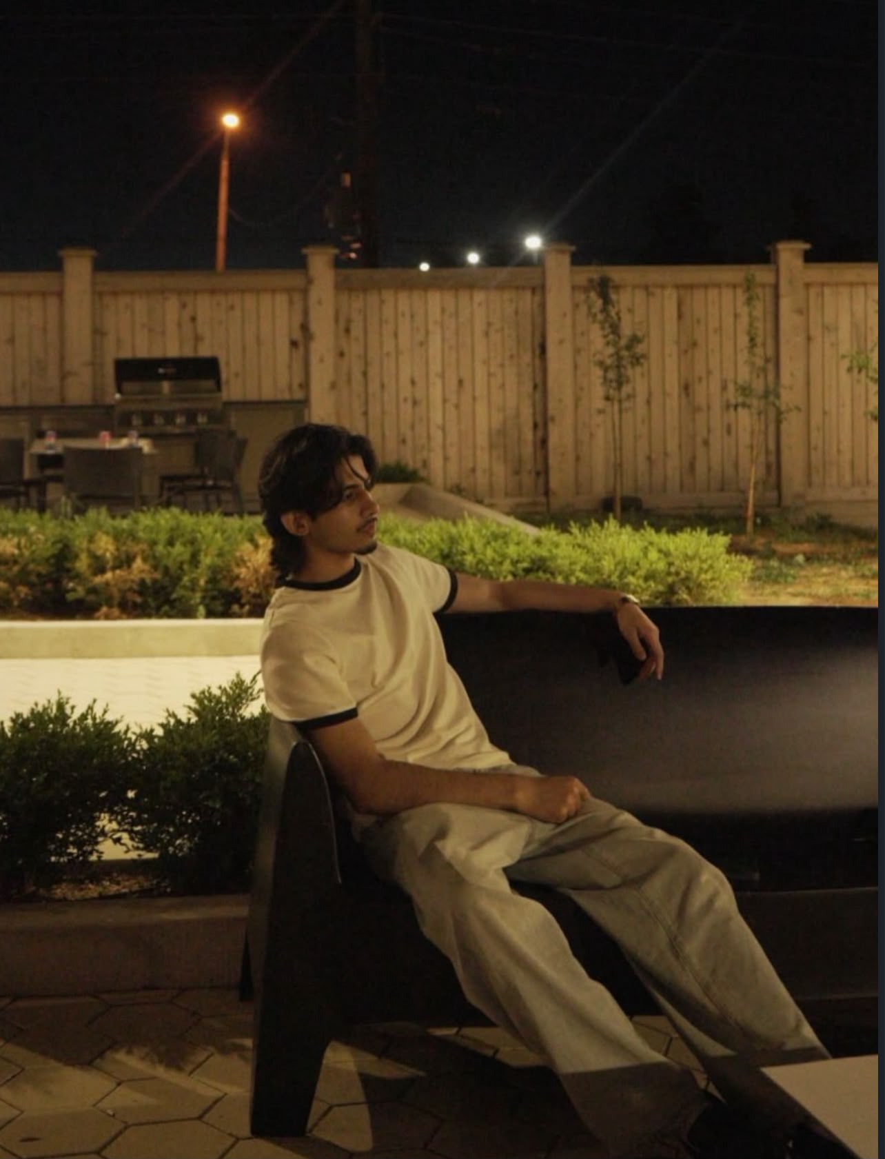 Seated outdoor portrait at night wearing a cream T-shirt and light trousers.