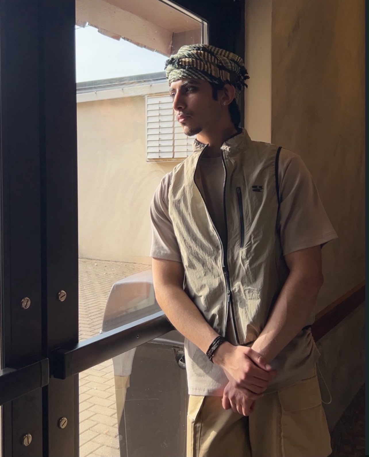 Portrait by a window wearing a beige vest and patterned headwrap.