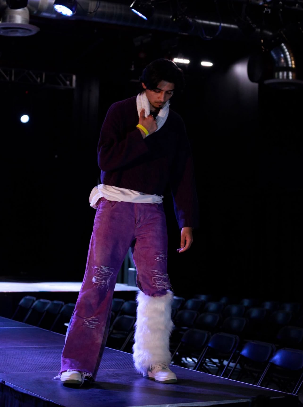 Modelling on a runway in a burgundy sweater and purple trousers.