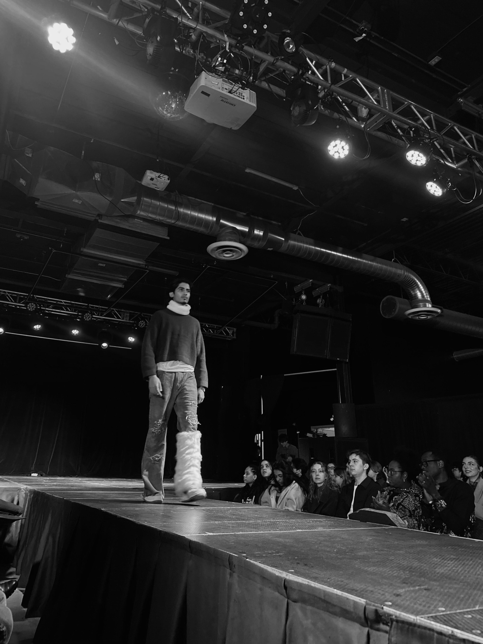 Black-and-white runway photograph with an audience beside the stage.